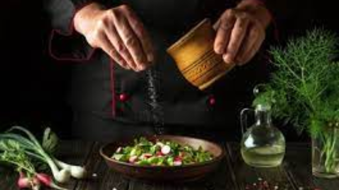 Chef preparing a fresh salad with herbs and vegetables while sprinkling salt, illustrating why do some chefs prefer kosher salt.
