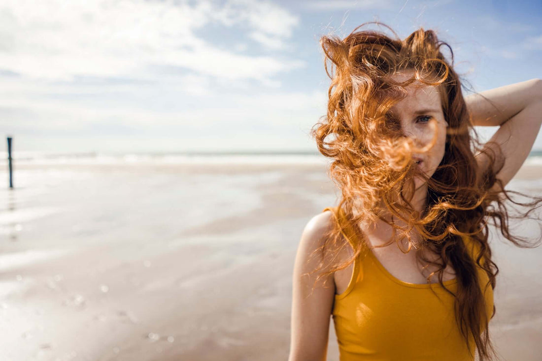 A woman with flowing red hair at the beach, embodying the style from DIY: Make a Sea Salt Hair Spray.